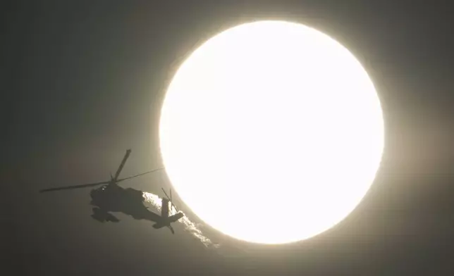 An Israeli Apache helicopter flies past the sun, near the Israeli-Lebanon border, as seen from northern Israel, Sunday, Oct. 13, 2024. (AP Photo/Leo Correa)