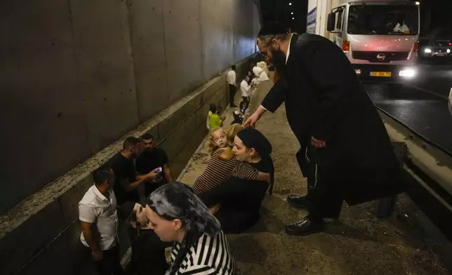 People take cover on the side of a road as a siren sounds a warning of incoming missiles fired from Iran on a freeway in Shoresh, between Jerusalem and Tel Aviv in Israel Tuesday, Oct. 1, 2024. (AP Photo/Ohad Zwigenberg)