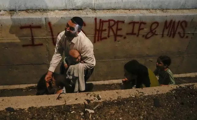 People take cover on the side of the road as a siren sounds a warning of incoming missiles fired from Iran on a freeway in Shoresh, between Jerusalem and Tel Aviv in Israel Tuesday, Oct. 1, 2024. (AP Photo/Ohad Zwigenberg)