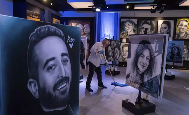 A worker cleans the floor at an exhibition by Israeli graffiti artist Benzi Brofman that displays portraits of the victims of the Oct. 7 Hamas attack on Israel, in Jerusalem, Sunday, Sept.29, 2024. (AP Photo/Ohad Zwigenberg)