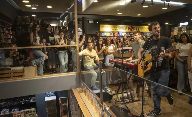 People listen to Israeli singer Yoni Bloch, who has written new songs about the current war, in concert at a record store in Tel Aviv, Israel, Friday, Sept. 27, 2024. (AP Photo/Ohad Zwigenberg)