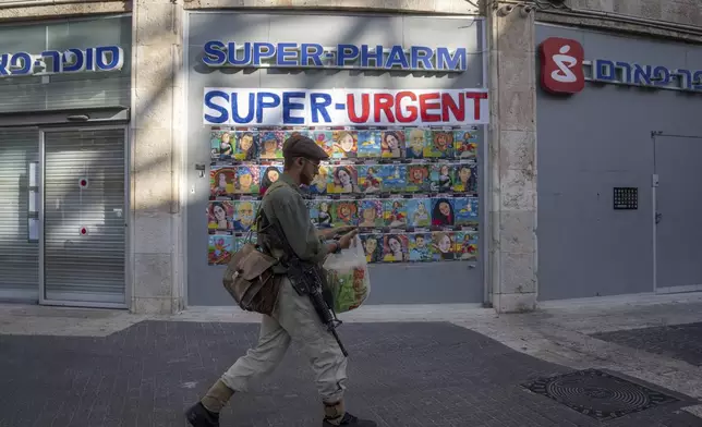 An off-duty Israeli soldier carrying his M-16 rifle walks past posters calling for the release of hostages held in the Gaza Strip, in Jerusalem, Friday, Sept.13, 2024. (AP Photo/Ohad Zwigenberg)