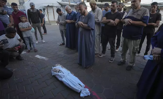 Mourners pray over the body of a Palestinian child, Hosam Al Khaldi, killed in the Israeli bombardment of the Gaza Strip outside the hospital morgue in Deir al-Balah on Wednesday, Oct. 9, 2024. (AP Photo/Abdel Kareem Hana)