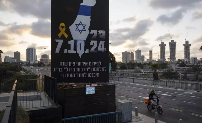 A man rides his bicycle next to a billboard with information about upcoming events marking the one-year anniversary of the Oct. 7 Hamas attack on Israel, in Tel Aviv, Israel, on Saturday, Oct. 5, 2024. (AP Photo/Oded Balilty)