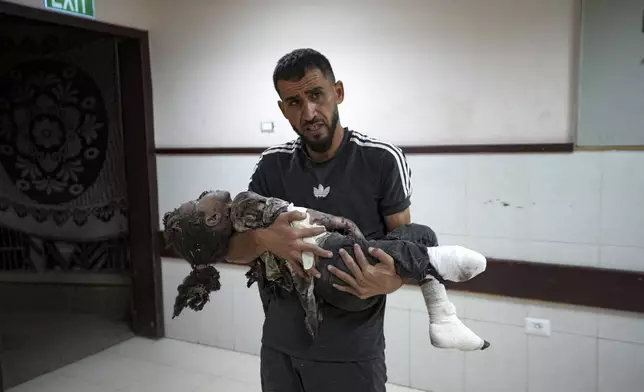 A Palestinian man holds a child wounded in the Israeli bombardment of the Gaza Strip in a hospital in Deir al-Balah, Monday, Sept. 30, 2024. (AP Photo/Abdel Kareem Hana)