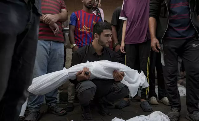 A Palestinian man holds the body of a relative killed in the Israeli bombardment of the Gaza Strip at a hospital morgue in Deir al-Balah, Tuesday, Oct. 8, 2024. (AP Photo/Abdel Kareem Hana)