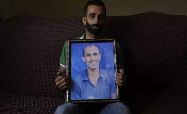 Palestinian Alaa al-Najjar holds a framed photo of his late brother Eyad al-Najjar, 47, at the family house in the West Bank village of Khalet al-Maya, east of Yatta Wednesday, Sept. 18, 2024. (AP Photo/Mahmoud Illean)