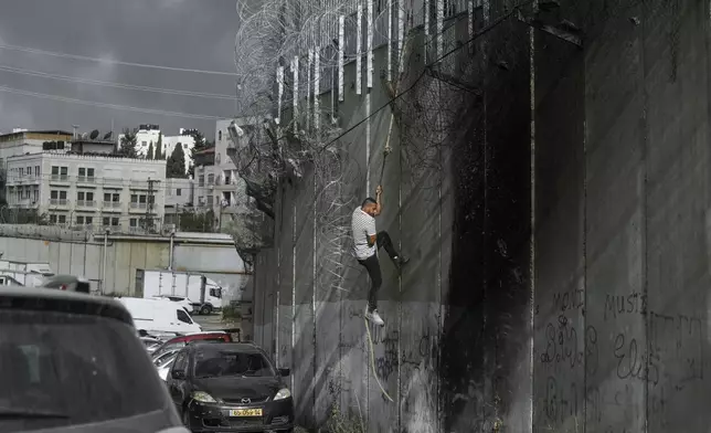 A Palestinian man climbs the separation wall at the town of al-Ram to illegally cross into Jerusalem, Sunday, Sept. 15, 2024. (AP Photo/Mahmoud Illean)