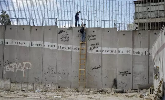 Palestinian men climb the separation wall at the town of al-Ram to illegally cross into Jerusalem, Sunday, Sept. 15, 2024. (AP Photo/Mahmoud Illean)