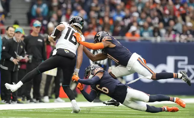 Jacksonville Jaguars quarterback Trevor Lawrence (16) is tackled by Chicago Bears safety Kevin Byard III (31) and cornerback Kyler Gordon (6) during an NFL football game at the Tottenham Hotspur stadium between the Jacksonville Jaguars and Chicago Bears in London, Sunday, Oct. 13, 2024. (AP Photo/Alastair Grant)