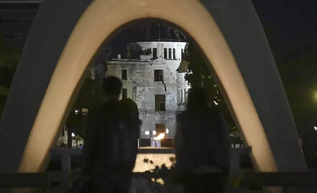 Visitors stand in front of the cenotaph for Atomic Bomb Victims at the Peace Memorial Park with the Atomic Bomb Dome seen in the background in Hiroshima, western Japan Friday, Oct. 11, 2024, after the Nobel Peace Prize was awarded to Nihon Hidankyo, a Japanese organization of survivors of the U.S. atomic bombings of Hiroshima and Nagasaki, for its activism against nuclear weapons. (Kyodo News via AP)