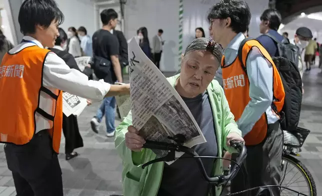 A person reads a copy of an extra version as workers of the Yomiuri Shimbun newspaper hand out its copies to passersby in Tokyo, Friday, Oct. 11, 2024, after Nihon Hidankyo, or the Japan Confederation of A- and H-Bomb Sufferers Organizations, won the Nobel Peace Prize. (AP Photo/Shuji Kajiyama)