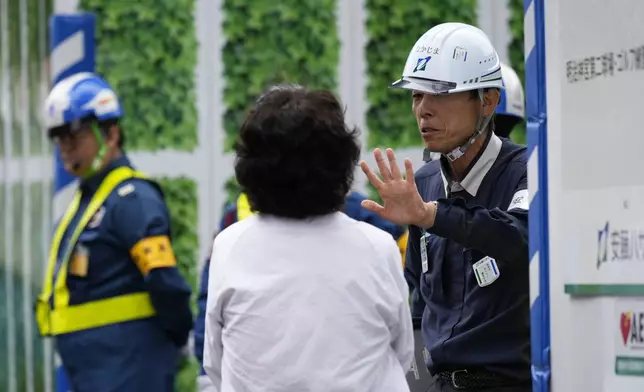 A worker, right, asks Mikiko Ishikawa, a university professor who protests against tree cutting, back to camera, to move out of a cordoned area in front of the Jingu Gaien park district of central Tokyo, Japan, where property developer Mitsui Fudosan begins cutting trees as part of the redevelopment work, Monday, Oct. 28, 2024. (AP Photo/Hiro Komae)