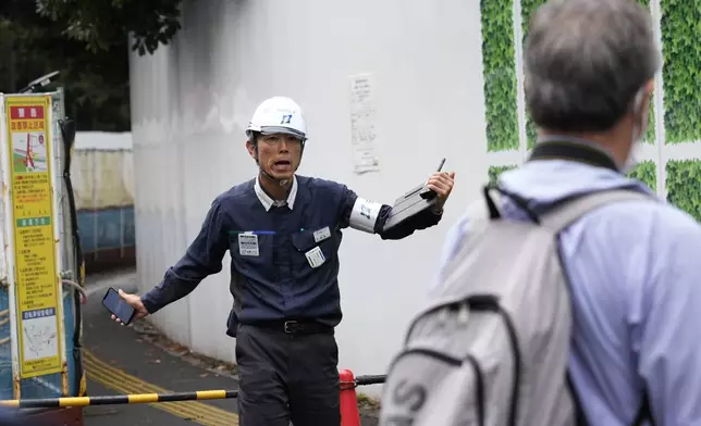 A worker, left, asks protesters and media members to move out of a cordoned area as environmentalists hold a rally near the Jingu Gaien park district of central Tokyo, Japan, to protest against property developer Mitsui Fudosan beginning cutting trees as part of the redevelopment work, Monday, Oct. 28, 2024. (AP Photo/Hiro Komae)