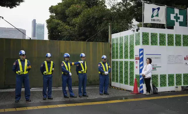 Mikiko Ishikawa, a university professor who protests against tree cutting stands right, as security guards stand in front of a gate of the Jingu Gaien park district of central Tokyo, Japan, where property developer Mitsui Fudosan begins cutting trees as part of the redevelopment of the area, Monday, Oct. 28, 2024. (AP Photo/Hiro Komae)