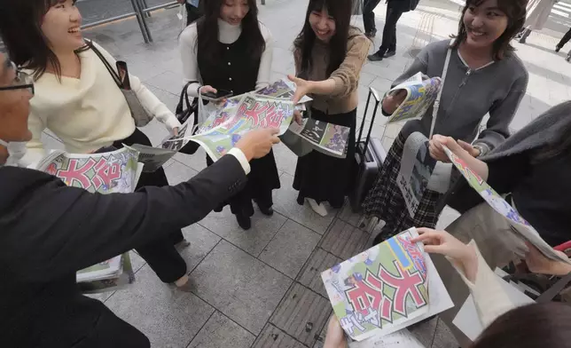 A staff member, left, distributes copies of an extra edition of the Sports Nippon newspaper in Tokyo, Thursday, Oct. 31, 2024, reporting on the Los Angeles Dodgers' victory in the World Series baseball match after the Dodgers defeated the New York Yankees in Game 5 in New York. (AP Photo/Eugene Hoshiko)