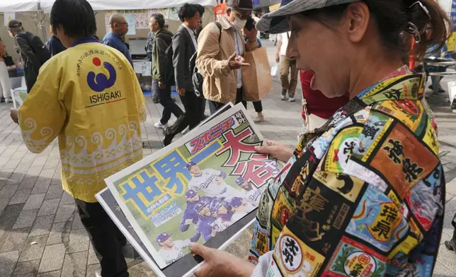 A passerby holds a copy of an extra edition of the Sports Nippon newspaper in Tokyo, Thursday, Oct. 31, 2024, reporting on the Los Angeles Dodgers' victory in the World Series baseball match after the Dodgers defeated the New York Yankees in Game 5 in New York. (AP Photo/Eugene Hoshiko)