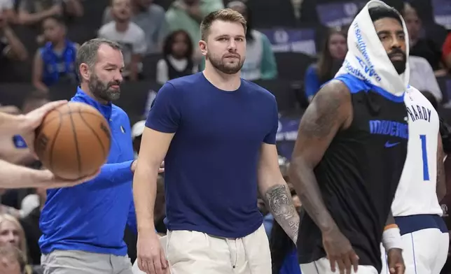 An injured Dallas Mavericks guard Luka Doncic, center, looks on from the sidelines as teammate Kyrie Irving, right, walks off during the first half of a preseason NBA basketball game against the Utah Jazz Thursday, Oct. 10, 2024, in Dallas. (AP Photo/LM Otero)