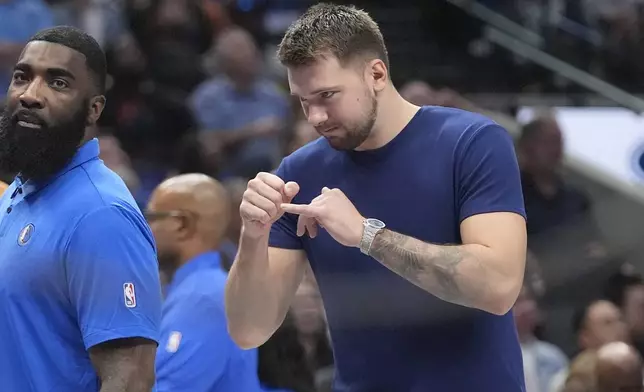 An injured Dallas Mavericks guard Luka Doncic, right, watches from the sidelines during a timeout in the first half of a preseason NBA basketball game against the Utah Jazz Thursday, Oct. 10, 2024, in Dallas. (AP Photo/LM Otero)