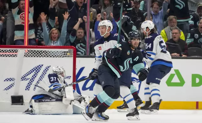 Seattle Kraken center Matty Beniers, front center, celebrates his goal against Winnipeg Jets goaltender Connor Hellebuyck (37) during the third period of an NHL hockey game Thursday, Oct. 24, 2024, in Seattle. (AP Photo/Lindsey Wasson)