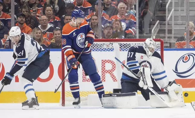 Winnipeg Jets goalie Connor Hellebuyck (37) makes a save as Edmonton Oilers' Zach Hyman (18) and Jets' Haydn Fleury (24) look on during the first period of an NHL hockey game, Wednesday, Oct. 9, 2024 in Edmonton, Alberta. (Amber Bracken/Canadian Press via AP)