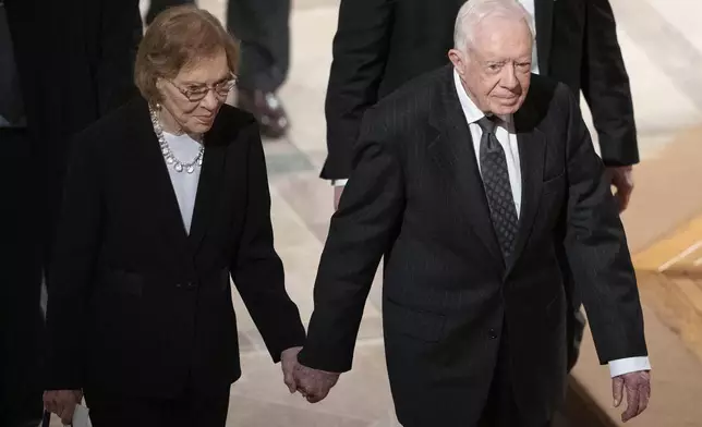 FILE - Former President Jimmy Carter, right, and his wife, former first lady Rosalynn Carter, hold hands as they walk from a state funeral for former President George H.W. Bush at the National Cathedral, Dec. 5, 2018, in Washington. (AP Photo/Carolyn Kaster, File)