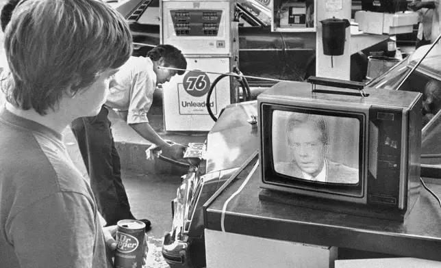 FILE - College student Chuck McManis watches President Jimmy Carter's nationally televised energy speech from a service station in Los Angeles, as a gas station attendant fills up a customer's car, July 15, 1979. (AP Photo/Mao, File)