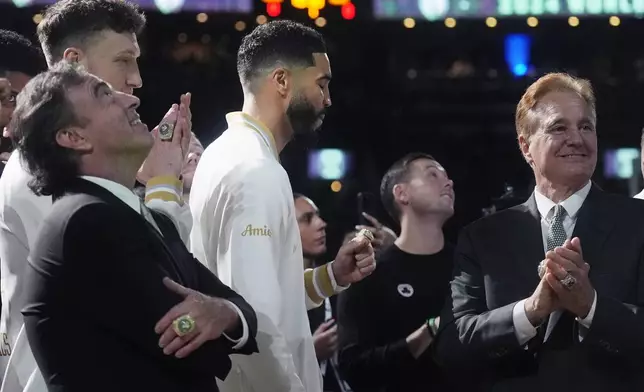 Boston Celtics forward Jayson Tatum, center, admires his ring as the 2024 World Championship banner is raised prior to an NBA basketball game against the New York Knicks, Tuesday, Oct. 22, 2024, in Boston. With Tatum are team owners Wyc Grousbeck, left, and Steve Pagliuca. (AP Photo/Charles Krupa)