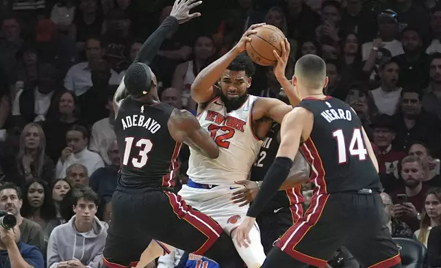 Miami Heat center Bam Adebayo (13) and guard Tyler Herro (14) defend New York Knicks center Karl-Anthony Towns (32) during the second half of an NBA basketball game, Wednesday, Oct. 30, 2024, in Miami. (AP Photo/Lynne Sladky)