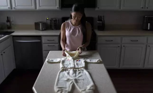 Leah Elmquist stands with the outfit she traveled in when she was adopted from Korea at five months old to a family in America, Monday, June 24, 2024, at her home in Las Vegas. (AP Photo/David Goldman)