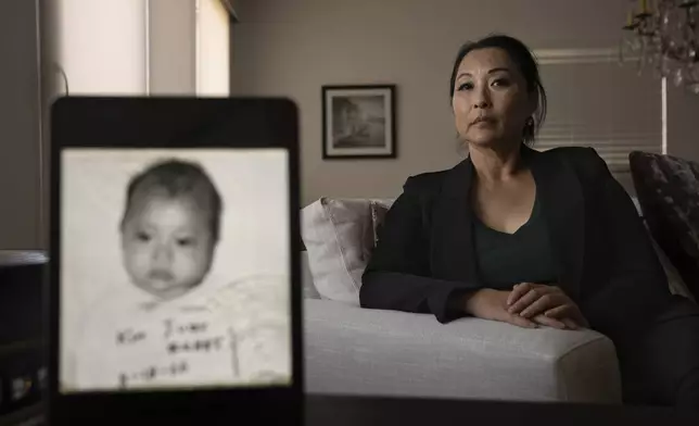 Joy Alessi sits for a portrait behind her baby picture from before she was adopted from South Korea to a family in America, Tuesday, June 25, 2024, in Henderson, Nev. (AP Photo/David Goldman)