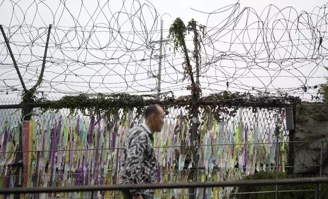 A visitor walks near a wire fence decorated with ribbons written with messages wishing for the reunification of the two Koreas at the Imjingak Pavilion in Paju, South Korea, Tuesday, Oct. 15, 2024. (AP Photo/Lee Jin-man)