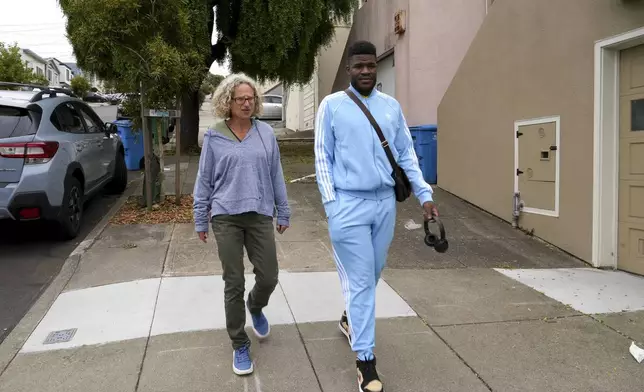 CORRECTS SPELLING OF LAST NAME Cabrel Ngounou, right, a refugee from Cameroon, walks with his sponsor Anne Raeff, in San Francisco, Tuesday, Sept. 17, 2024. (AP Photo/Terry Chea)