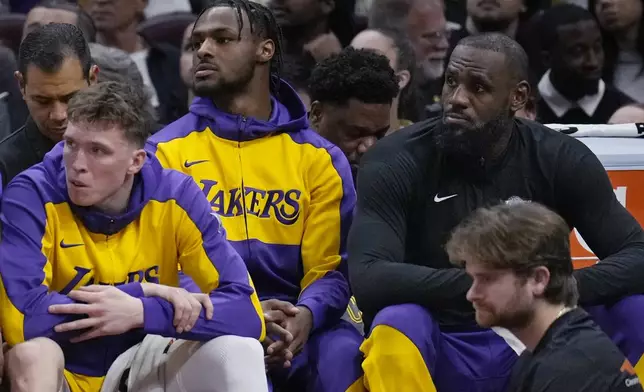 Los Angeles Lakers guard Bronny James, center, and forward LeBron James, right, watch from the bench with guard Dalton Knecht, left, in the first half of an NBA basketball game against the Cleveland Cavaliers, Wednesday, Oct. 30, 2024, in Cleveland. (AP Photo/Sue Ogrocki)