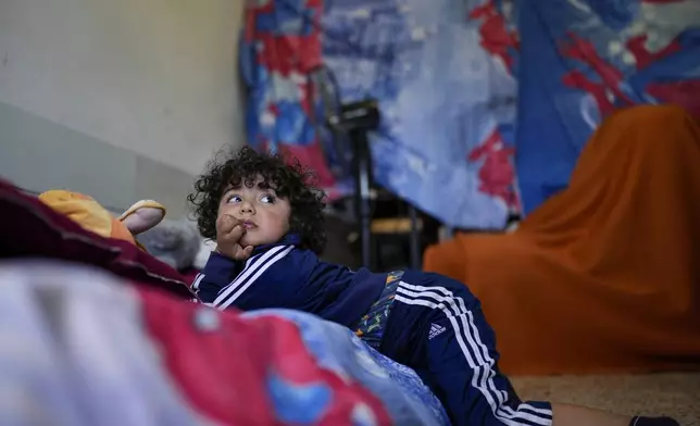 A displaced child who fled southern Lebanon with relatives during the ongoing Hezbollah-Israel war watches television inside a classroom in the village of Ebrine, northern Lebanon, Thursday, Oct. 24, 2024. (AP Photo/Hassan Ammar)