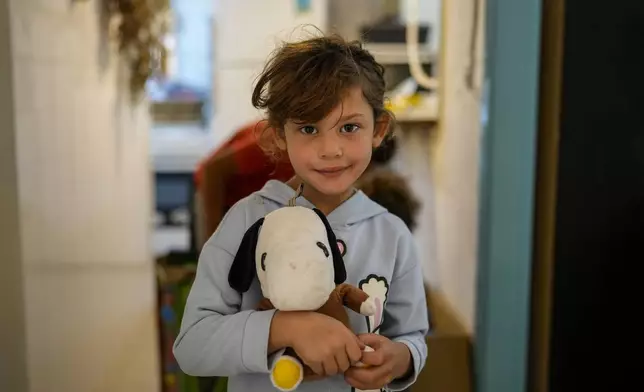 A displaced girl who fled southern Lebanon during the ongoing Hezbollah-Israel war poses for a photograph with her toy at a women's art center that has turned into a kitchen for displaced people, in the town of Aqaibe, northern Lebanon, Thursday, Oct. 24, 2024. (AP Photo/Hassan Ammar)