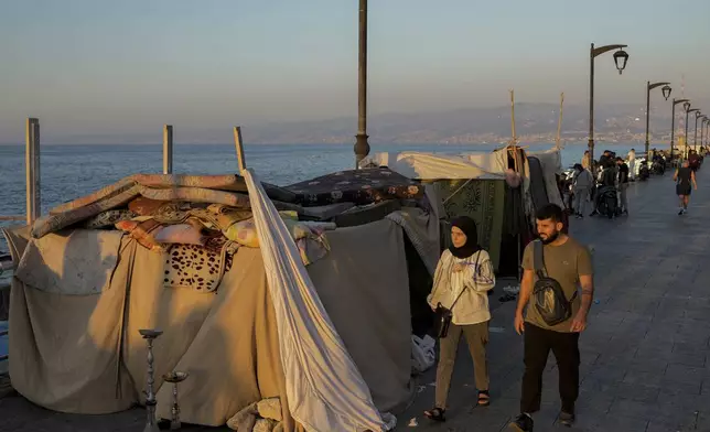 People walk past tents set up as temporary shelters by displaced families fleeing the Israeli airstrikes in the south and Dahiyeh, on Beirut's corniche, Lebanon, Tuesday Oct. 8, 2024. (AP Photo/Bilal Hussein)