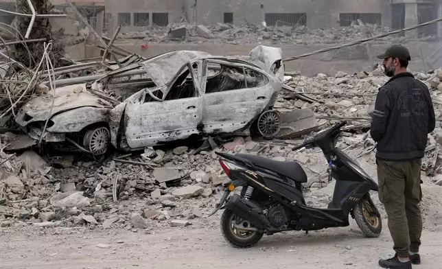 A man stands in front of a destroyed car at a scene hit by Israeli airstrikes in Dahiyeh, Beirut, Lebanon, Monday, Oct. 7, 2024. (AP Photo/Hussein Malla)