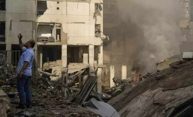 A man documents the damaged buildings at the site of an Israeli airstrike in Beirut's southern suburb, Lebanon, Tuesday, Oct. 1, 2024. (AP Photo/Hassan Ammar)