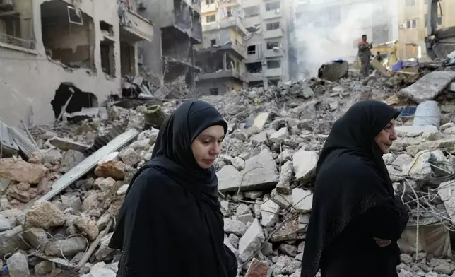 Lebanese women pass the destroyed buildings hit by an Israeli airstrike, in Beirut, Lebanon, Friday, Oct. 11, 2024. (AP Photo/Hussein Malla)