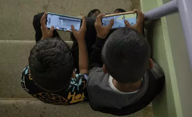 Displaced children play games on their mobile phone at a vocational training center run by the U.N. agency for Palestinian refugees, or UNRWA, in the southern town of Sebline, south of Beirut, Lebanon, Friday, Oct. 4, 2024, after fleeing the Israeli airstrikes in the south. (AP Photo/Bilal Hussein)