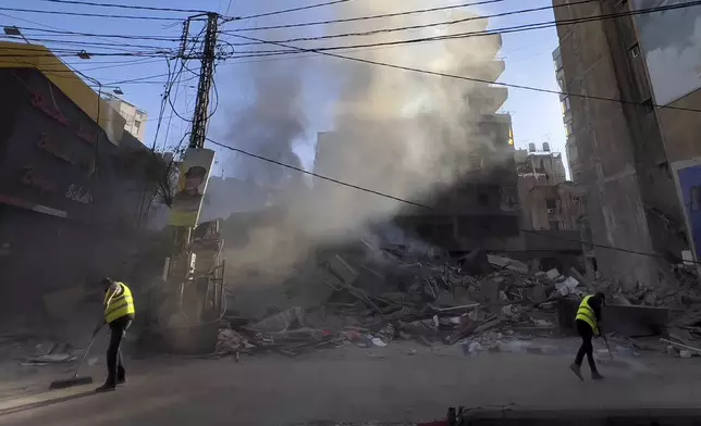 Workers clean a street as smoke rises from a destroyed building that was hit by an Israeli airstrike in Dahiyeh, a southern suburb of Beirut, Lebanon, early Sunday, Oct. 20, 2024. (AP Photo/Hussein Malla)