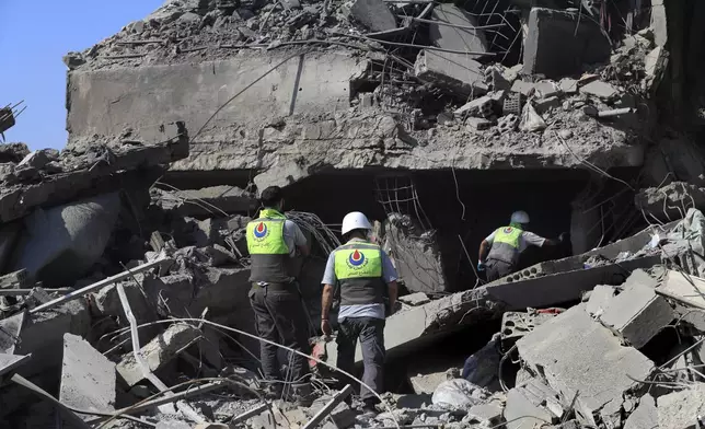 Hezbollah rescue workers search for victims on the rubble of destroyed buildings at commercial street that was hit Saturday night by Israeli airstrikes, in Nabatiyeh town, south Lebanon, Sunday, Oct. 13, 2024. (AP Photo/Mohammed Zaatari)