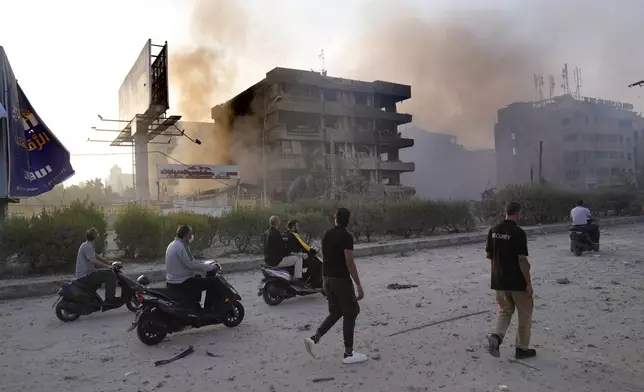 People pass in front of destroyed buildings that were hit by Israeli airstrikes in Dahiyeh, Beirut, Lebanon, Sunday, Oct. 6, 2024. (AP Photo/Hussein Malla)