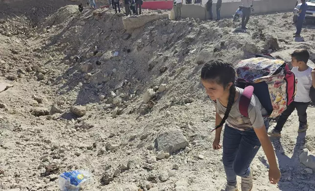 A girl carries her belongings crossing on foot into Syria through a crater caused by an Israeli airstrike to cut the road between the Lebanese and the Syrian checkpoints, at the Masnaa crossing, in the eastern Bekaa Valley, Lebanon, Friday, Oct. 4, 2024. (AP Photo/Samer Husseini)