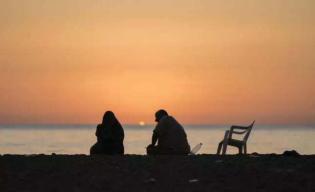 A displaced couple sits at Ramlet al-Baida public beach after fleeing the Israeli airstrikes in the south, as the sun sets over the Mediterranean Sea in Beirut, Lebanon, Tuesday, Oct. 8, 2024. (AP Photo/Bilal Hussein)