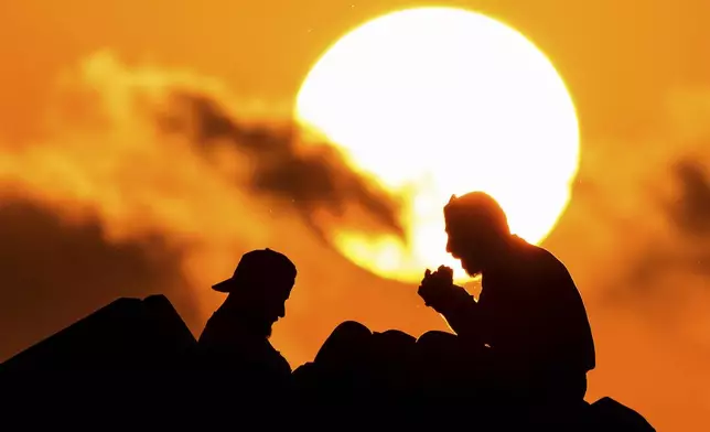 Displaced men fleeing the Israeli airstrikes in Beirut's Dahiyeh suburb, eat as sit at Beirut's seaside promenade, along the Mediterranean Sea while the sun sets over the capital Beirut, Lebanon, Thursday, Oct. 17, 2024. (AP Photo/Hassan Ammar)