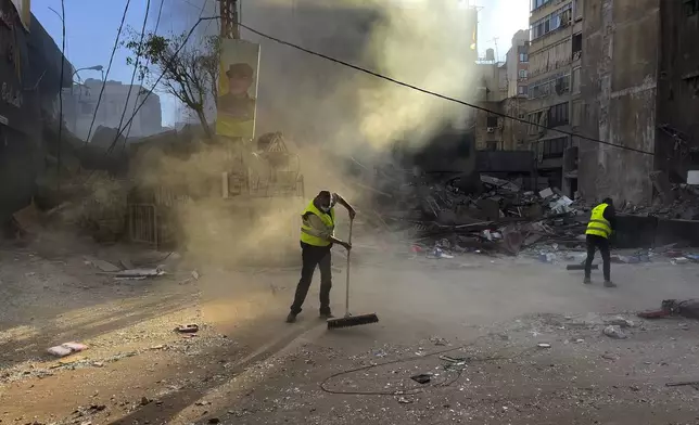 Workers clean a street as smoke rises from a destroyed building that was hit by an Israeli airstrike in Dahiyeh, in the southern suburb of Beirut, Lebanon, early Sunday, Oct. 20, 2024. (AP Photo/Hussein Malla)