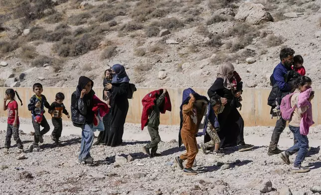 Families cross into Syria on foot, through a crater caused by Israeli airstrikes aiming to block Beirut-Damascus highway at the Masnaa crossing, in the eastern Bekaa Valley, Lebanon, Saturday, Oct. 5, 2024. (AP Photo/Hassan Ammar)