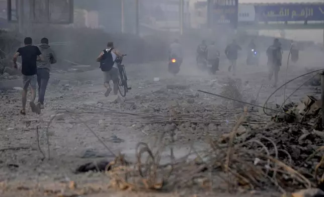 People run from a warplane sound on the debris of destroyed buildings hit by Israeli airstrikes in Dahiyeh, Beirut, Lebanon, Sunday, Oct. 6, 2024. (AP Photo/Hussein Malla)